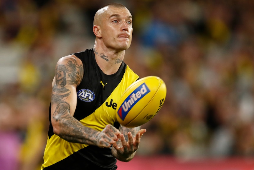 A Richmond Tigers AFL player handballs with his right hand. 