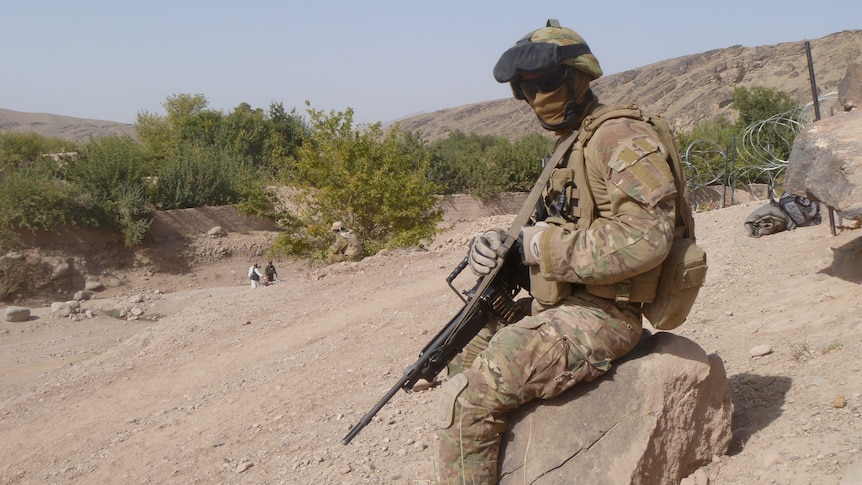 a soldier sits on a rock in the desert