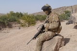 a soldier sits on a rock in the desert
