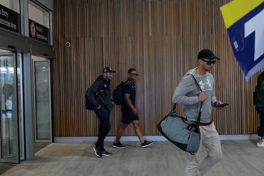 Valentine Holmes memakai kacamata hitam berjalan keluar dari gerbang keamanan di dalam terminal bandara.