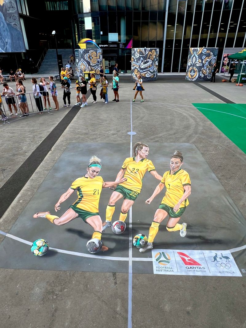 A large chalk mural of three Matildas soccer players kicking a ball drawn on the ground at Marvel Stadium. 