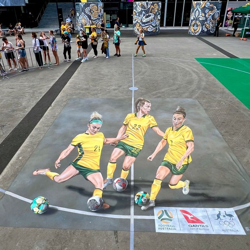 A large chalk mural of three Matildas soccer players kicking a ball drawn on the ground at Marvel Stadium. 