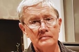 A tight head and shoulders profile shot of Ian Collett indoors wearing a brown shirt and spectacles.