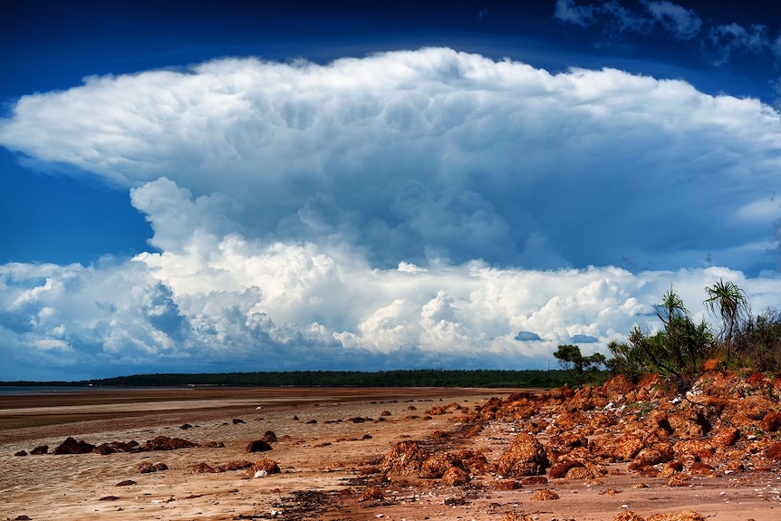 Massive storm cloud brews over a red dirt coastline