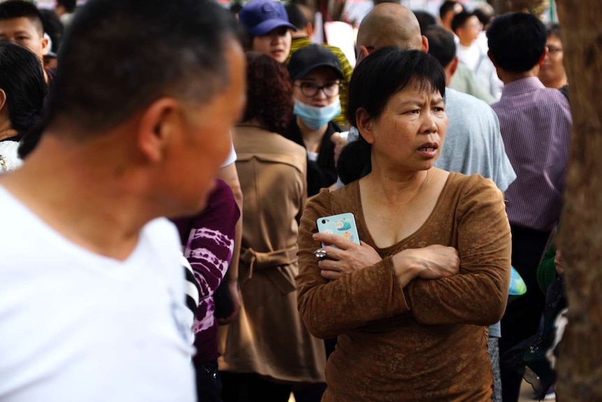 Woman with arms folded ampng the crowd of people at the market.