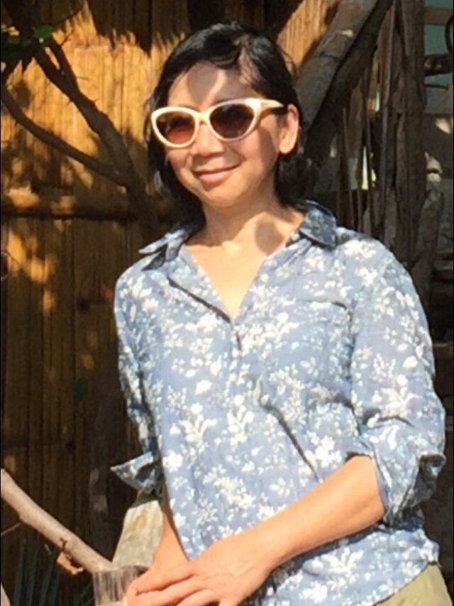 A woman in sunglasses smiles wearing a blue floral shirt.