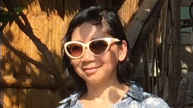 A woman in sunglasses smiles wearing a blue floral shirt.