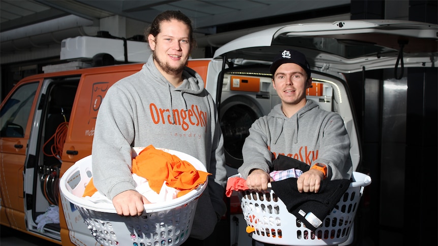 Nick Marchesi and Lucas Patchett hold washing baskets in front of a wash van.