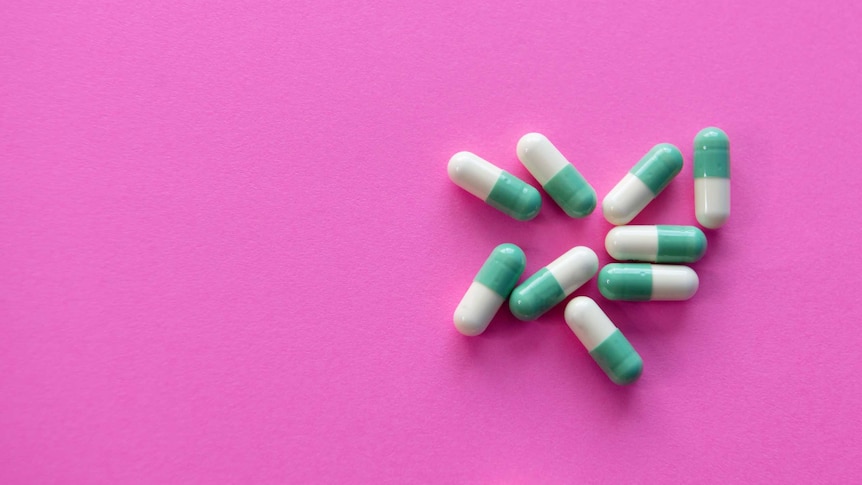 A handful of pills (capsule medications) against a pink backdrop