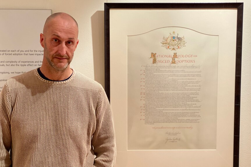 Picture of Abe Maddison standing in front of framed picture of the national apology