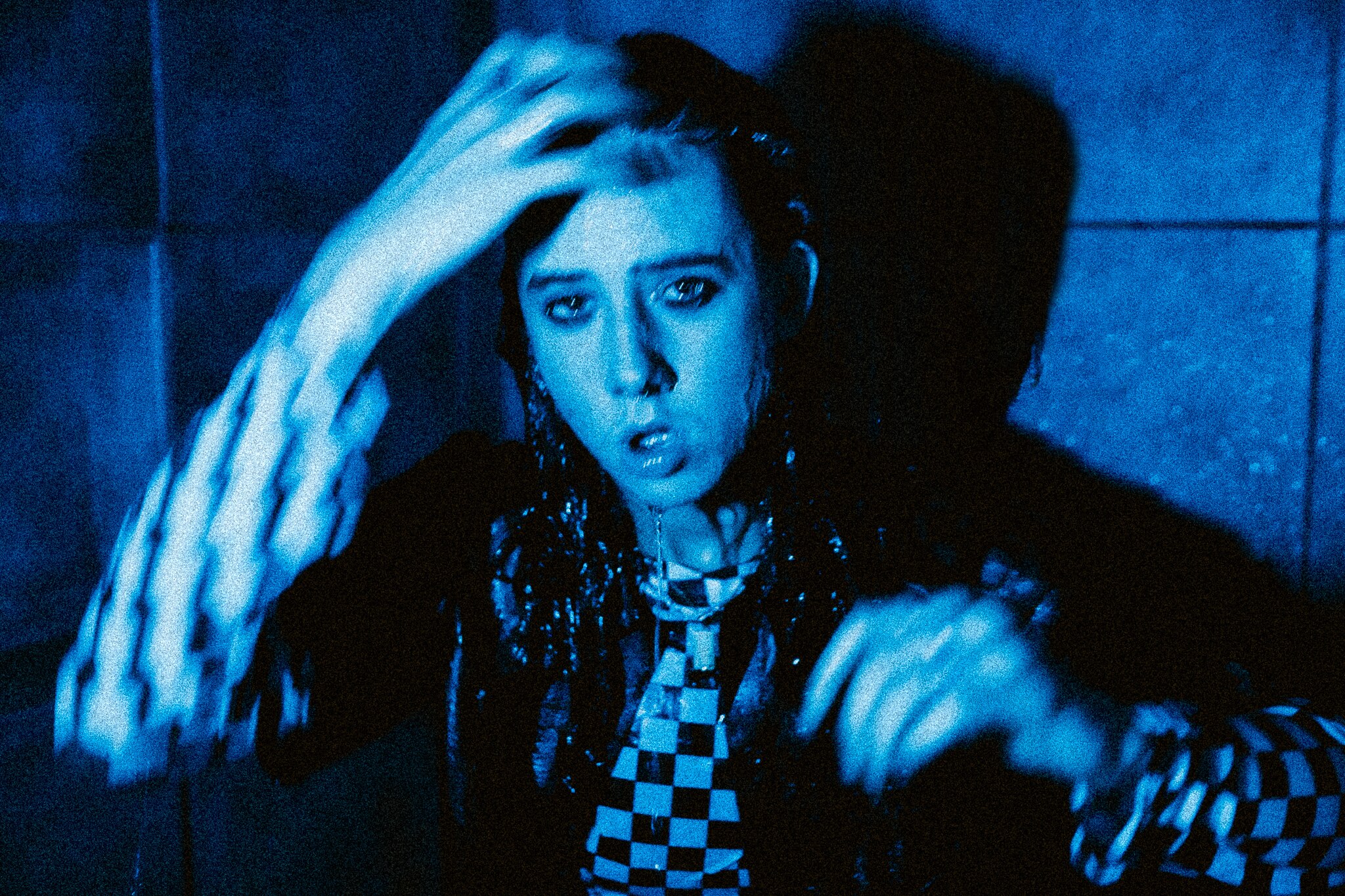 Black and blue static image of Chloe Dadd dripping wet in a checkered shirt in a bathroom