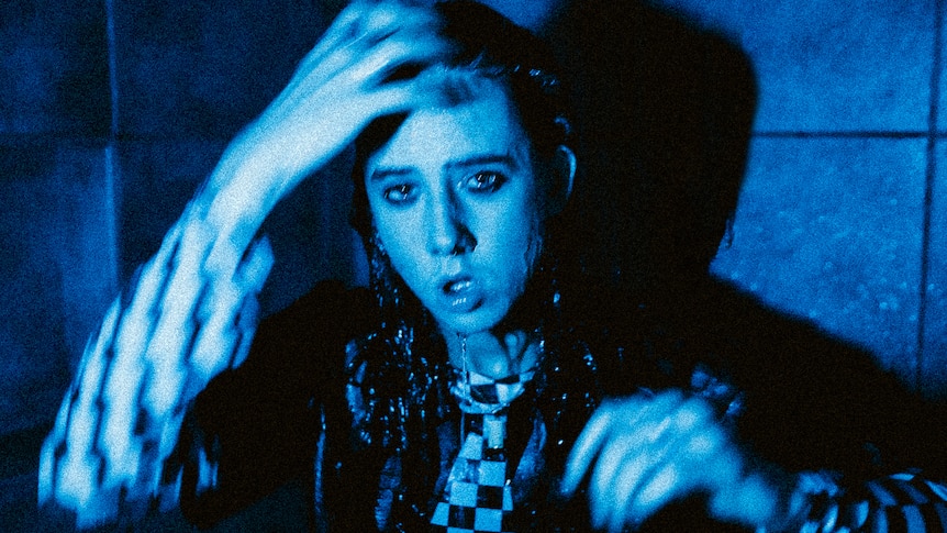 Black and blue static image of Chloe Dadd dripping wet in a checkered shirt in a bathroom