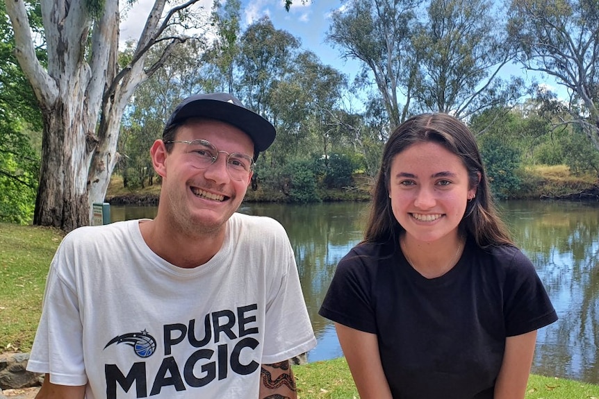A young man and woman sit by the banks of the Murray River.