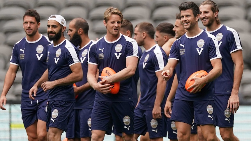A collection of Victoria players stand around and chat happily at training.