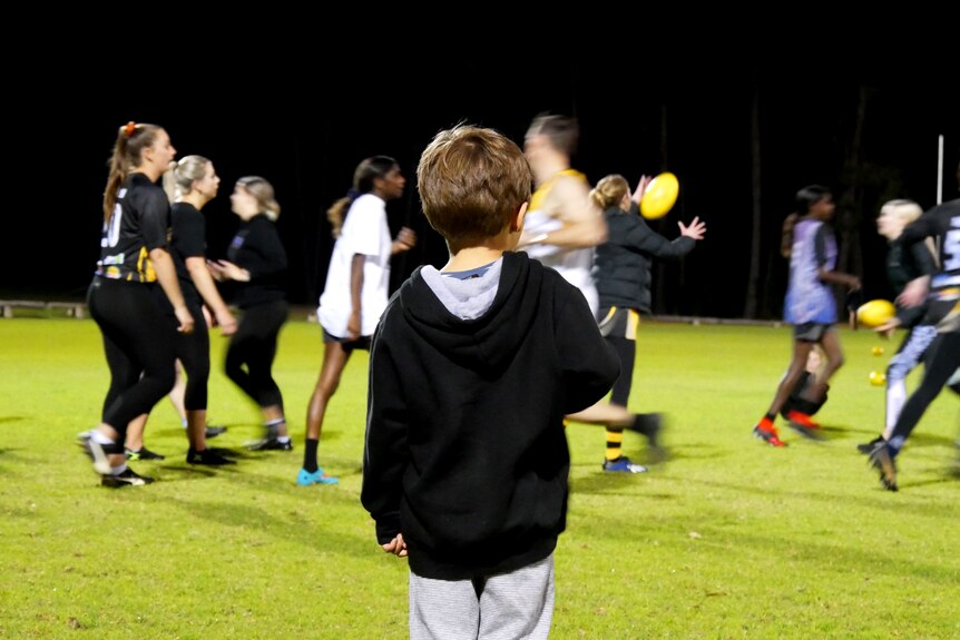 A young boy watches a women's AFL training session., 