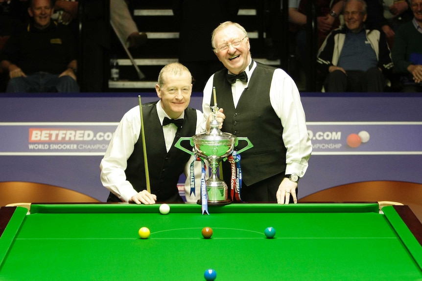 Steve Davis and Dennis Taylor smile and pose next to a silver trophy