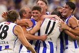 A group of North Melbourne players hug and celebrate together