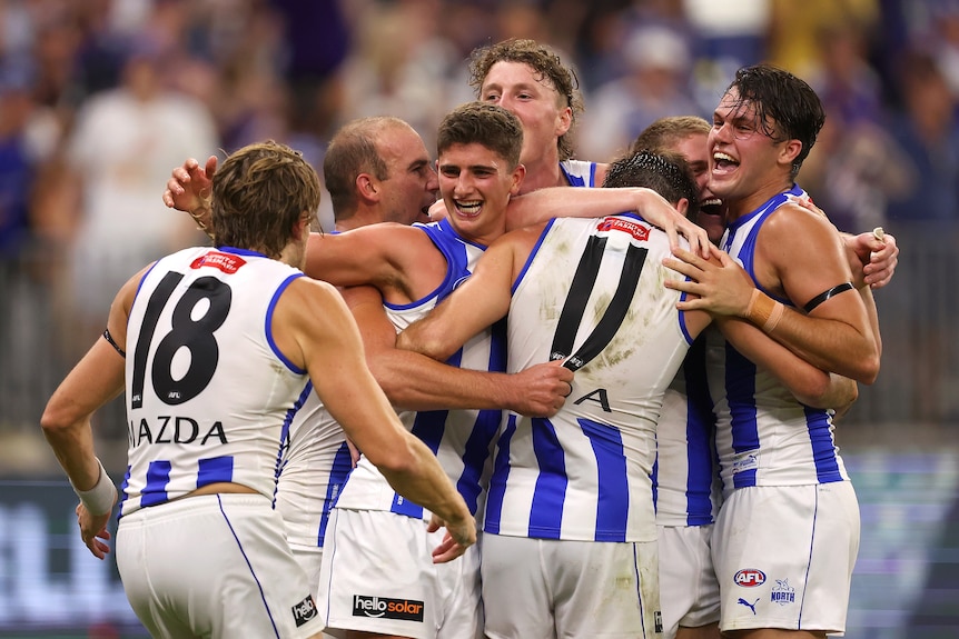 A group of North Melbourne players hug and celebrate together