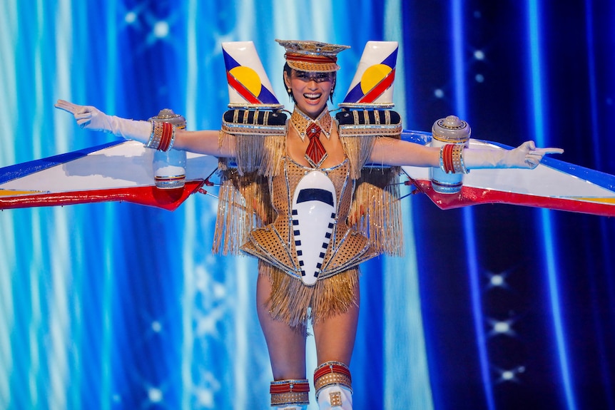 Michelle Dee wearing a splarkly gold captains hat and a costume that has the wings of a plane