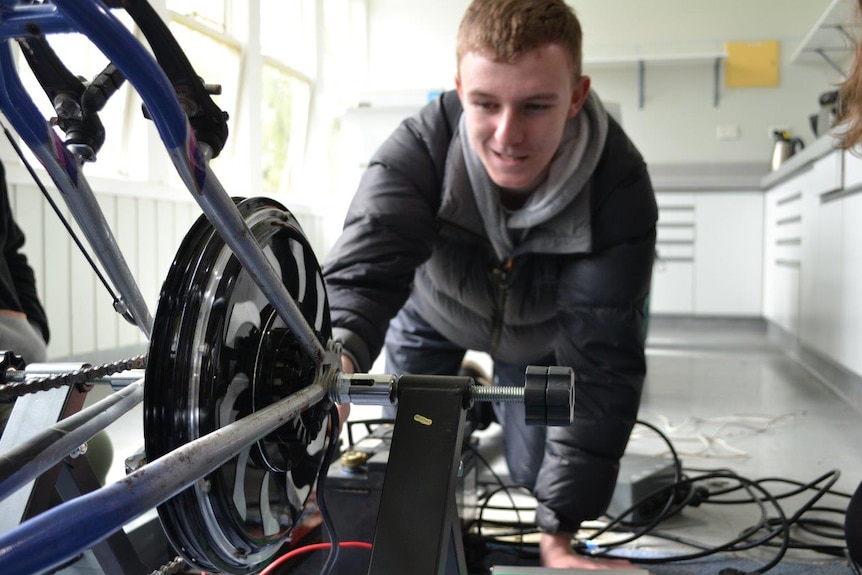 Toby Thorpe working on a bicycle which Huonville High School hopes will eventually power a cinema