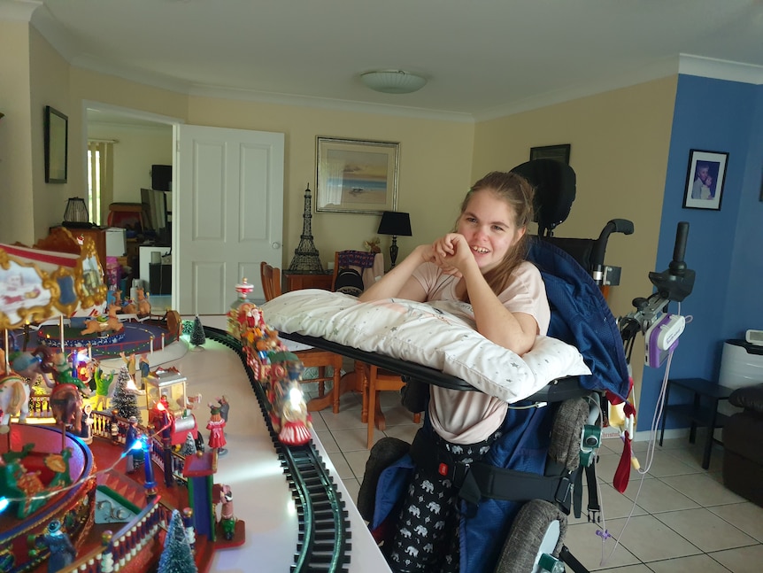 Tara Ingerson watches a model train set, smiling in her wheelchair. 