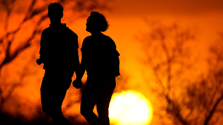 A couple walks through a park at sunset