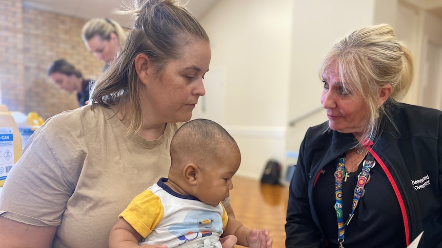 A woman sits with her son on her lap while a nurse gives her information about the vaccines he's about to receive.