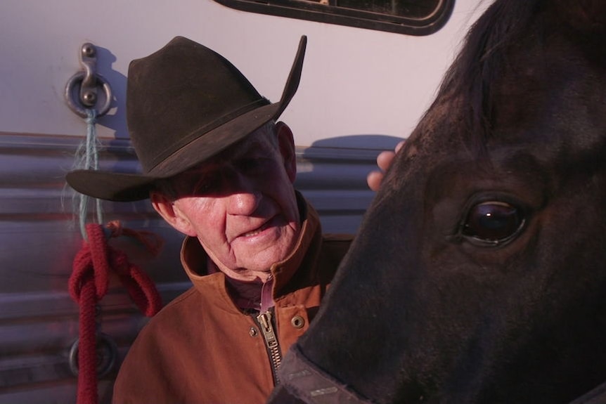 A man wearing a cowboy hat pats a horse.