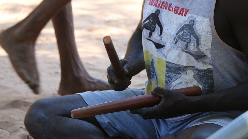 A man plays rhythm sticks at an Indigenous funeral ceremony at Elcho Island.