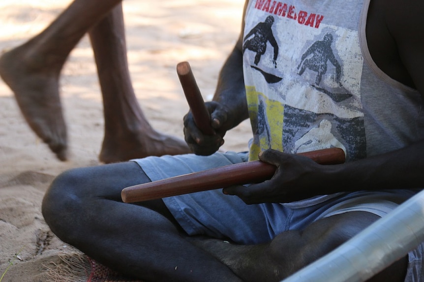 A man plays rhythm sticks at an Indigenous funeral ceremony at Elcho Island.