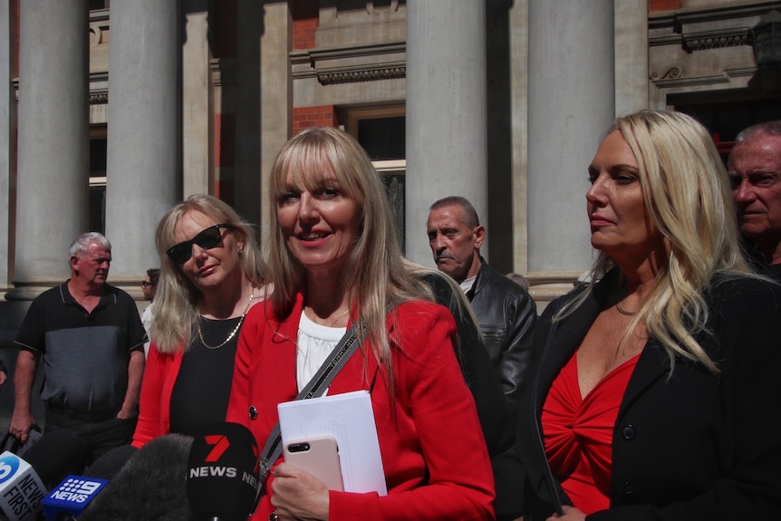 A group of blonde women speak outside a large building.
