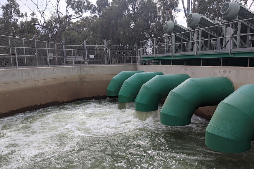 Five large green cylinders point downward into a deep pool. Two of the cylinders are pumping a large amount of water.