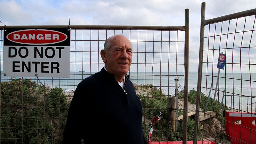 A man stands in front of fences with a "do not enter" sign stopping access to the beach.