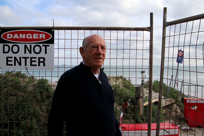A man stands in front of fences with a "do not enter" sign stopping access to the beach.