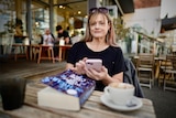 A woman with blonde hair sits at a coffee shop with a book.