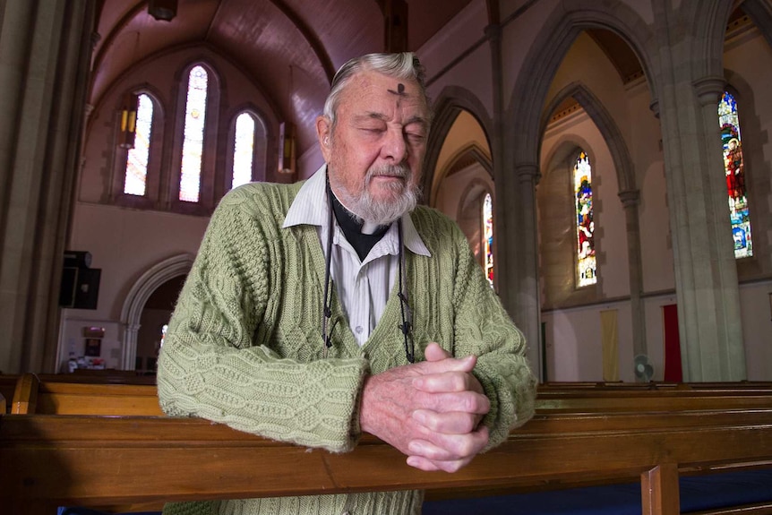 A man kneels at a pew in church, with a cross marked in ash on his forehead