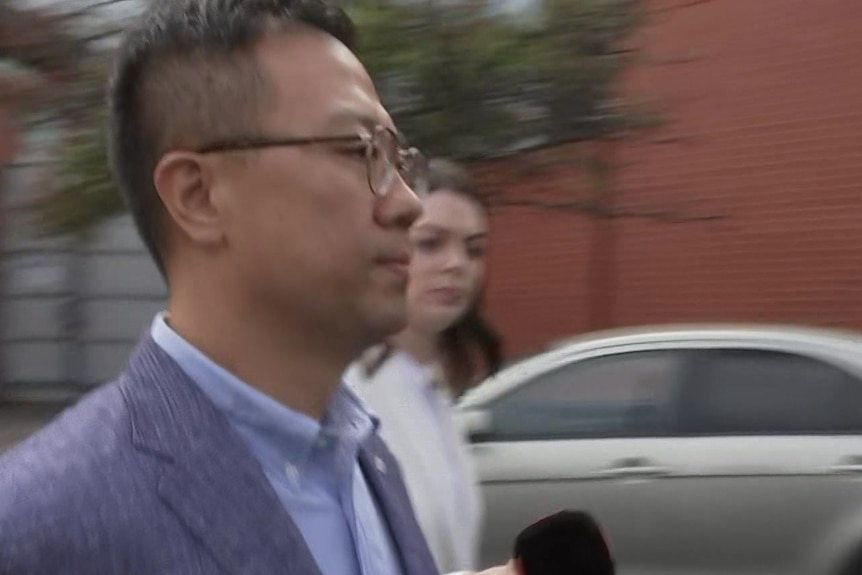 A side-on image of a man walking outside court, behind him is a woman holding a microphone towards him