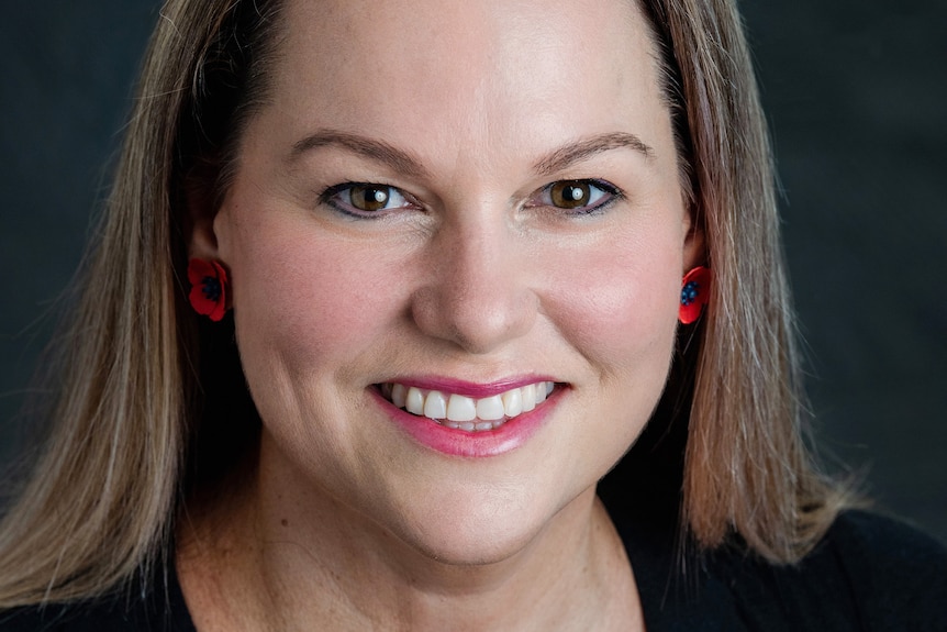 a professional headshot of a woman smiling, she is wearing earrings that look like poppies 