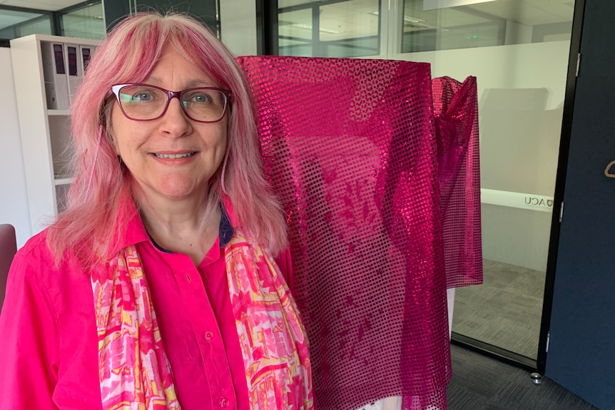 A middle-aged white woman wearing a pink shirt, scarf and glasses
