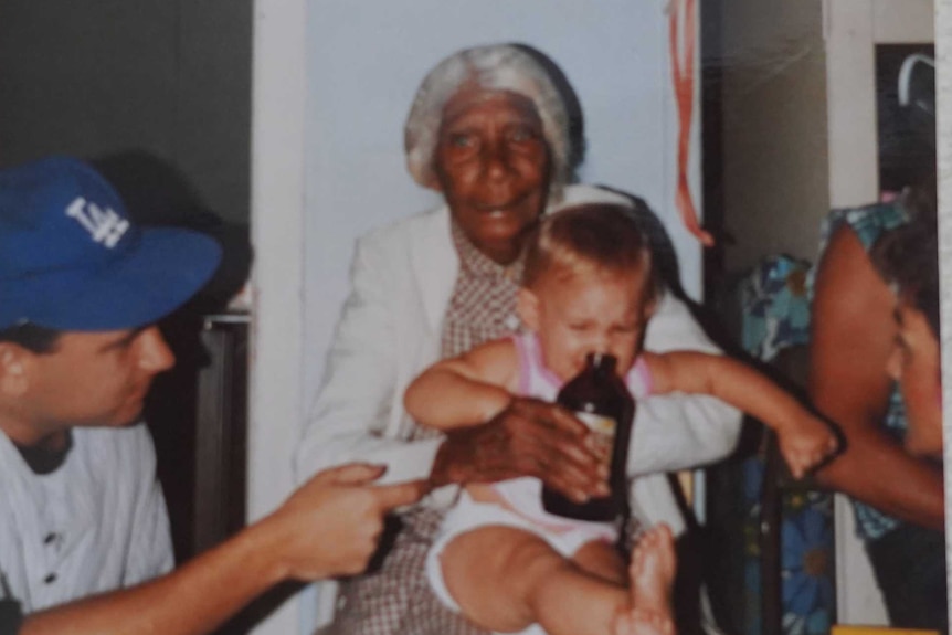 An elderly woman dandling light skinned grandchildren on her knee.
