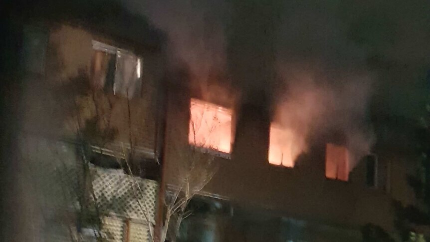 Flames and smoke can be seen through three windows at the top of a unit block.