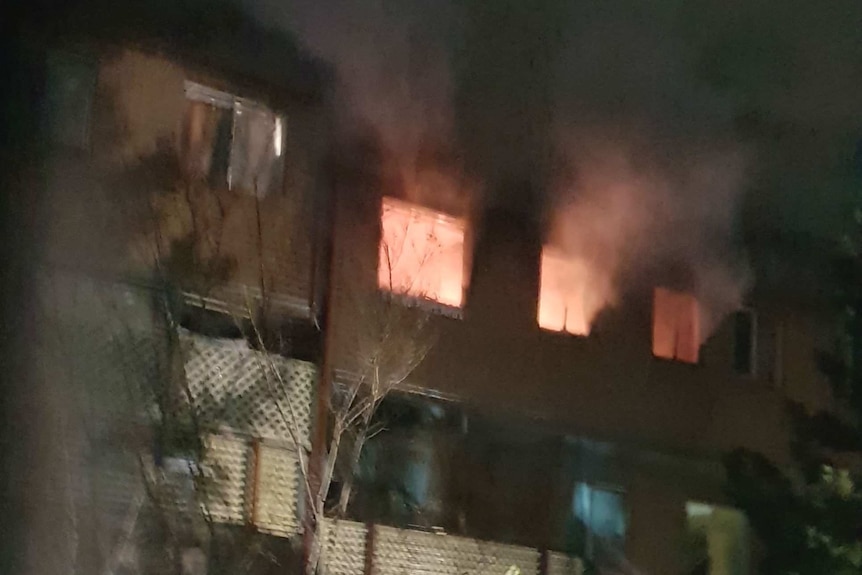 Flames and smoke can be seen through three windows at the top of a unit block.