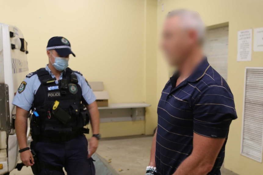 A police officer wearing a mask stands next to a man with a blurred face.