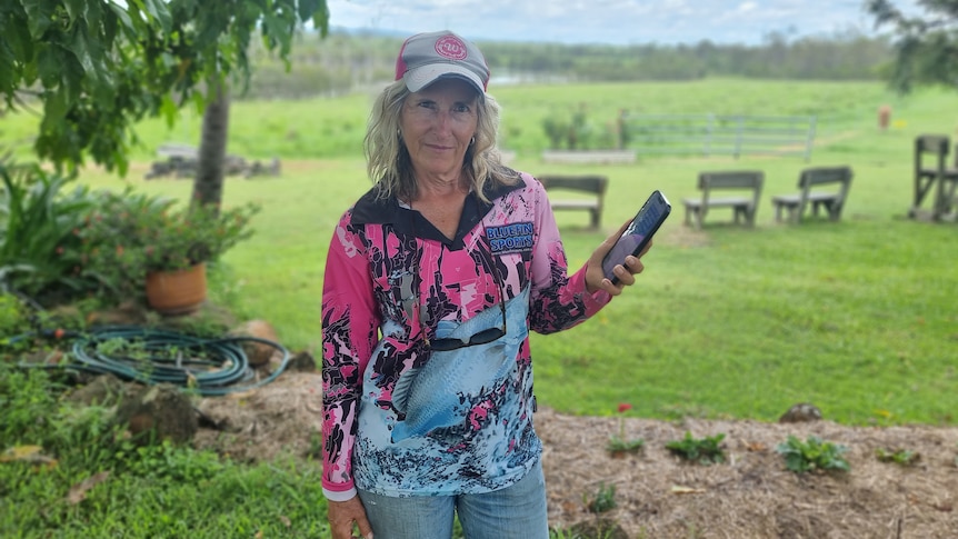 Wide shot of a woman standing in a garden holding her mobile phone