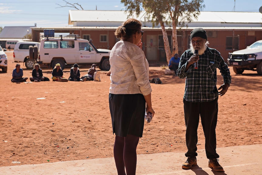 A man with a beard wearing a beanie talks into the microphone standing next to Leanne Liddle.