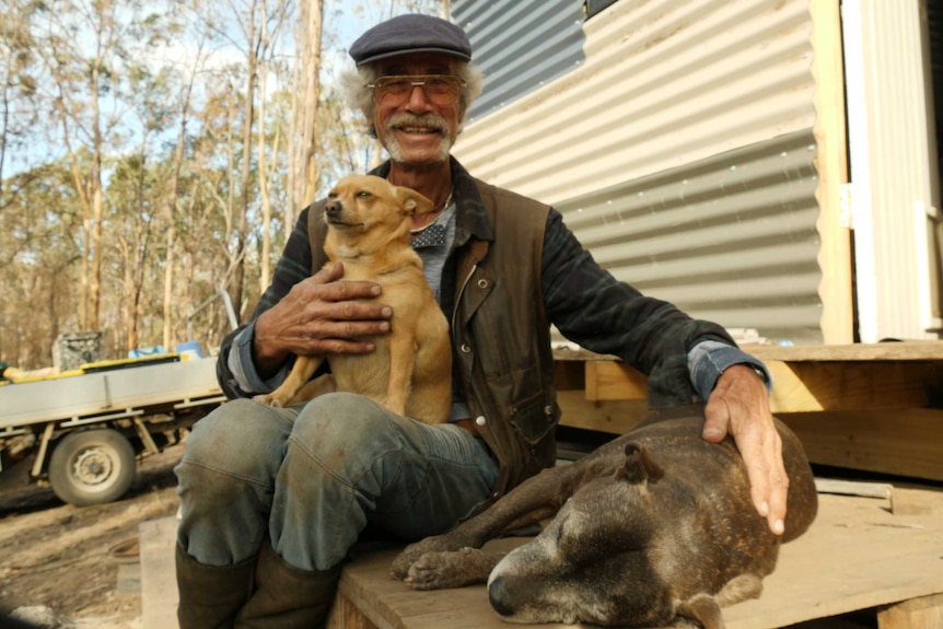 A man and his two dogs sit on the doorstep of a shed.