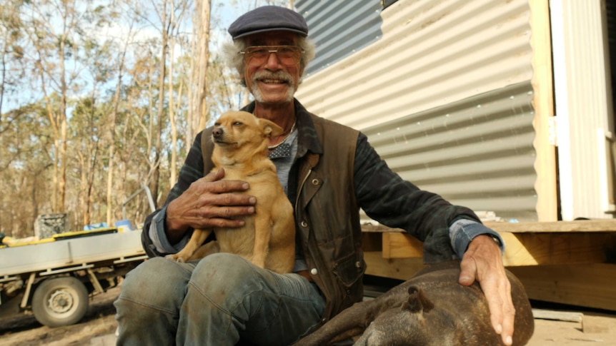 A man and his two dogs sit on the doorstep of a shed.