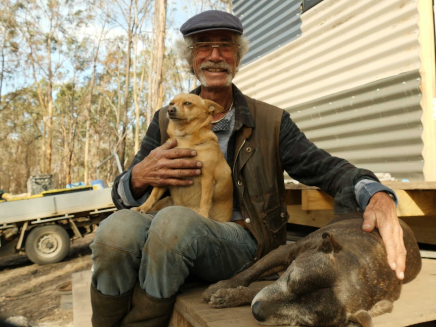 A man and his two dogs sit on the doorstep of a shed.
