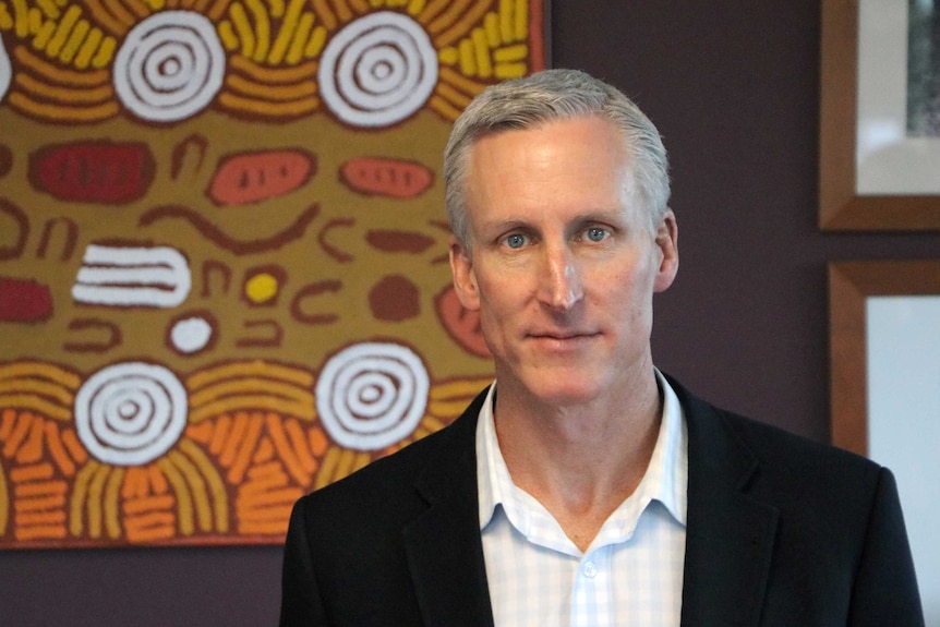 Tim Shackleton standing in front of an Aboriginal artwork.