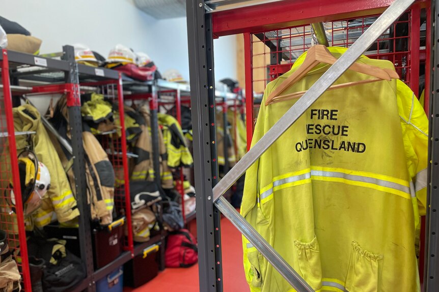 Fire gear hangs inside a station, one yellow jacket has Fire Rescue Queensland written on back.